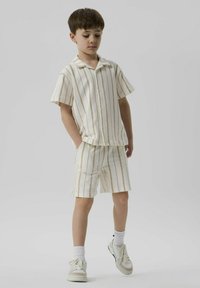 Kortsleeve ljuskrämfärgad skjorta och matchande shorts med vertikala beige ränder, tillverkad av textilerat tyg, fickor på shortsen, bärs med vita sneakers.