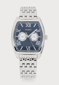 Montre en acier inoxydable argenté avec un cadran rectangulaire, un cadran bleu marine, des chiffres romains et deux plus petits cadrans. Elle est dotée d'un bracelet à style tissé.