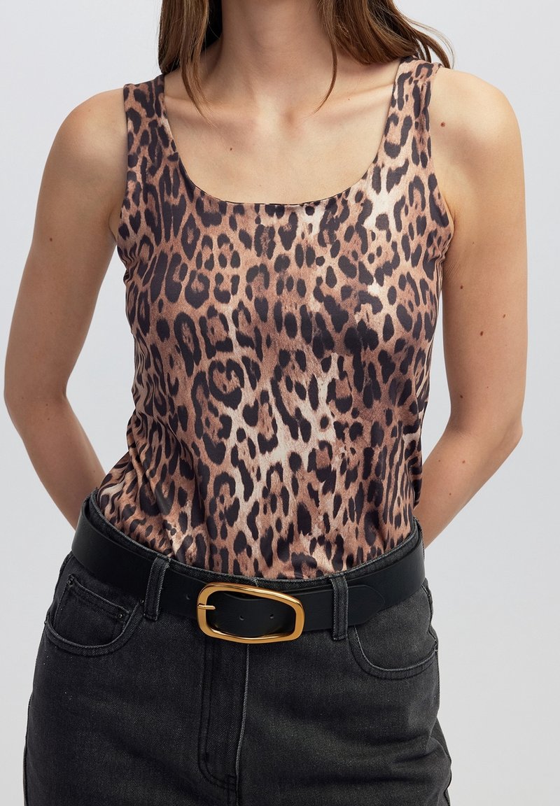 Femme portant un haut sans manches à imprimé léopard rentré dans un jean noir avec une ceinture noire à boucle dorée.