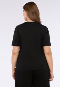 Camisa negra de manga corta con una textura suave. Presenta un cuello redondo y acentos estampados en los hombros. Estilo clásico ajustado.