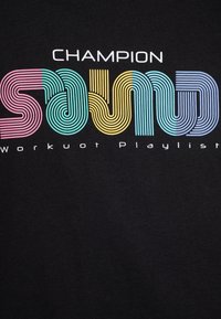 T-shirt noir en coton doté d'un texte en bandes multicolores audacieuses indiquant "CHAMPION SOUND Workout Playlist" dans des polices ludiques.