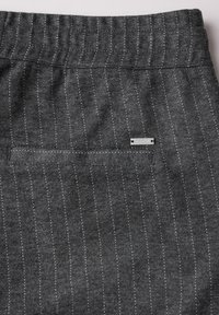 Pantalons en tissu gris avec des pinstripes blancs verticaux, dotés d'une taille élastique et d'une petite poche arrière avec une étiquette en métal.