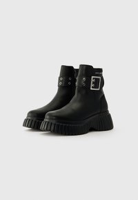 Black ankle boots made of leather with a chunky ribbed sole, featuring a silver buckle accent and side zipper for closure.