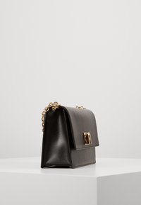 Sort læder håndtaske med et struktureret design, guld hardwarelås og en kædestrop. Tekstureret overflade med en flad rektangulær form.