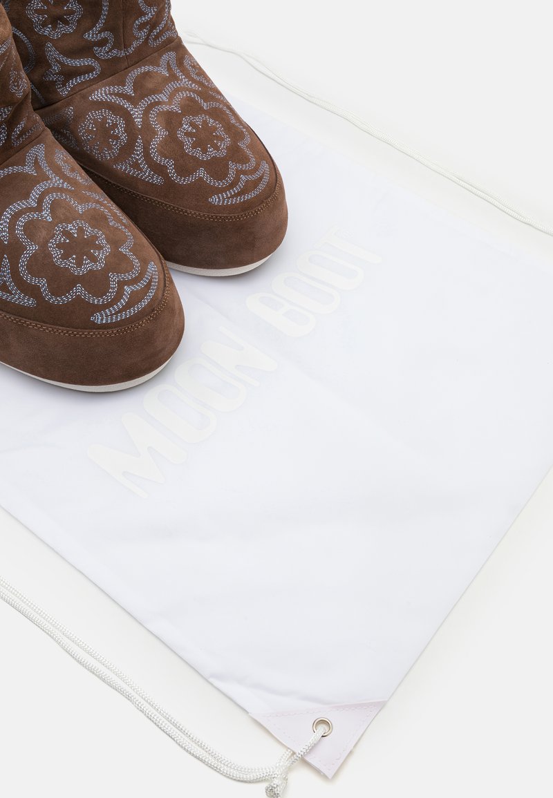 Brązowe zamszowe buty Moon Boot z kwiecistym haftem, w połączeniu z białą torbą na sznurku z nazwą marki w jasnoszarym kolorze.