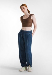 Bruine cropped tanktop, lichtblauwe denim, losse broek met een elastische tailleband en beige sneakers met groene accenten.