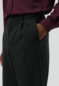 Grijs pantalon met krijtstreep, een getailleerde pasvorm, voorzien van zijzakken en een knoopsluiting, gecombineerd met een bordeauxrode blouse met lange mouwen.