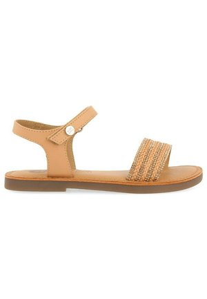 Sandale en cuir tan avec une sangle tressée présentant des accents métalliques, semelle plate et sangle de cheville ajustable. Design simple et minimaliste.