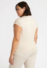Top beige de manga corta con un diseño ajustado, textura suave y detalles decorativos en los hombros, combinado con pantalones claros a juego.