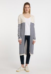 Cardigan a righe in crema e blu navale, maniche lunghe, apertura frontale, texture a maglia. Abbinato a un top bianco semplice e jeans scuri. Footwear casual.