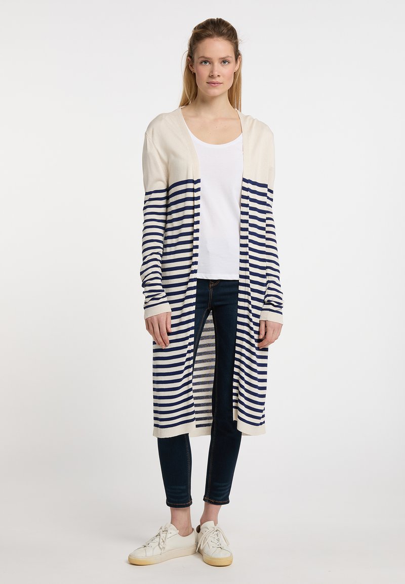Cardigan a righe in crema e blu navale, maniche lunghe, apertura frontale, texture a maglia. Abbinato a un top bianco semplice e jeans scuri. Footwear casual.