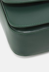 Grön läderväska med slät yta, rundade kanter och kontrasterande gröna sömmar. Har lager av fack för organisering.