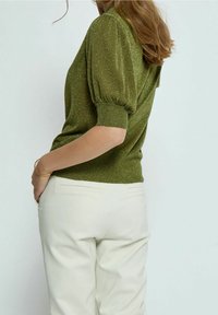 Grön, glittrig stickad tröja med puffade korta ärmar, ribbade muddar och fåll. Kombinerad med ljusa byxor med skräddarsydda detaljer.