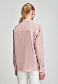 Camicia rosa chiaro in tessuto leggero e texture, con colletto e maniche lunghe. Presenta polsini con bottoni e una vestibilità morbida.