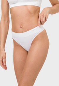 White cotton thong underwear with a soft waistband, featuring a seamless design and smooth texture. Logo text is embossed on the waistband.