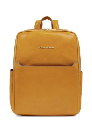 Mochila cuadrada de cuero color mostaza con bolsillo delantero, cierre de doble cremallera, asa superior y logo de la marca centrado en el panel frontal superior.