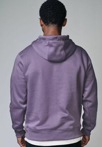 Felpa viola con cappuccio regolabile, polsini e fondo a costine, e una texture liscia. Mostrata da dietro, rivelando i dettagli delle cuciture.