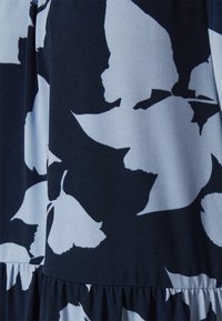 Tecido azul-marinho com um padrão floral branco, textura suave, design fluido e bainha com babado franzido. Detalhe em close do padrão.