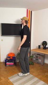 Zwart T-shirt, grijze spijkerbroek en zilveren sneakers. Oranje lamp en blauwe bijzettafel in een kamer met een houten vloer en kleurrijke muuraccenten.