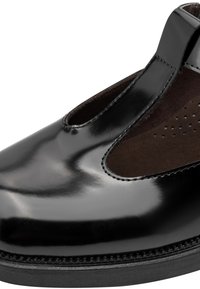 Gros plan d'une chaussure en cuir noir brillant avec un design à bride en T et un panneau en daim brun foncé perforé sur une semelle noire.