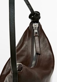 Brown leather bag with a curved shape, featuring a silver zipper and a black adjustable strap. The texture is smooth with a subtle sheen.