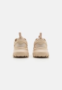 Beige sneakers med överdel i mesh, vadderad krage och dragflik. Tjock gummisula med texturerat mönster för grepp. Minimalistisk design.