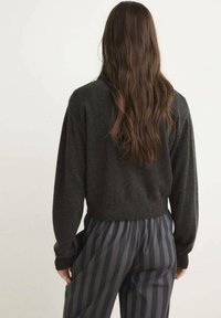 Dark gray knit sweater with a relaxed fit, featuring long sleeves and a ribbed hem, paired with gray striped trousers.