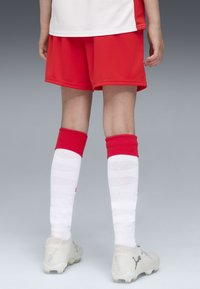 Röda sportshorts, vita strumpor med röda detaljer och vita fotbollsskor. Fokus på funktionalitet och komfort inom sportkläder.