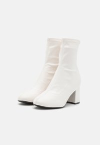 Bottes blanches chevilles en matériau lisse, à bout pointu et talon épais. Présentent une tige ajustée et extensible avec des détails de couture subtils.