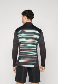 Langarm sportshirt in het zwart met een kleurrijk, gestreept ontwerp op de achterkant in teal, rood en wit; heeft een hoge kraag en een gestructureerde stof.