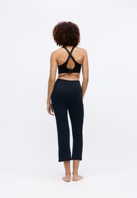 Soutien-gorge de sport noir avec des bretelles croisées et un dos découpé, associé à des leggings cropped ajustés de couleur bleu marine foncé. Texture lisse, design minimal.
