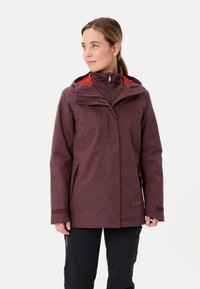 Giacca impermeabile color marrone con cappucci regolabili, tasche con zip e polsini elastici. Presenta un rivestimento rosso e un tessuto resistente per l'uso all'aperto.
