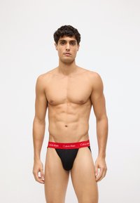 Crne tange s crvenim pojasom na kojem se nalazi logo "Calvin Klein". Glatka tekstura, konturirani dizajn i minimalna pokrivenost.