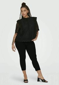 Top de renda preta com mangas franzidas, textura em camadas, combinado com capris pretas ajustadas e sandálias de salto bloco abertas.