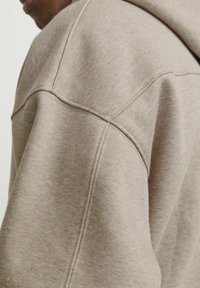 Beige hoodie featuring a soft, textured fabric with a close-up view showing structured seams and a relaxed fit design.