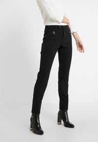 Svarta skräddarsydda byxor med slim fit och framfickor med dragkedja, kombinerat med svarta höga ankelstövlar. Slät tyg och minimalistisk design.