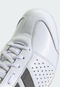 Białe skórzane buty sportowe o gładkiej fakturze, zaokrąglonym nosku, szarych akcentach, perforowanych sekcjach oraz płaskich białych sznurowadłach.