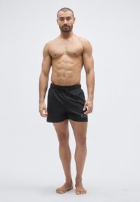 Fekete fürdőnadrág húzózsinóros derékrésszel, bal lábszáron logóval. Sima anyag, térd feletti hosszúság, további minták nélkül.