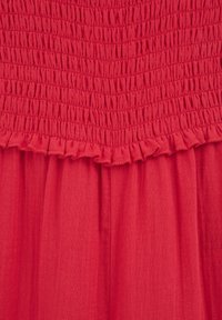 Red dress featuring a textured smocked bodice with a ruffled edge, flowing into a smooth skirt. Made from lightweight fabric.