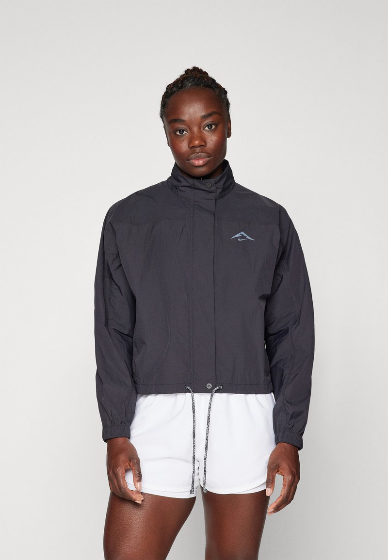 Schwarze Windjacke mit hohem Kragen, elastischen Bündchen, Kordelzugsaum und einem blauen Logo-Akzent. Leichter, glatter Stoff.