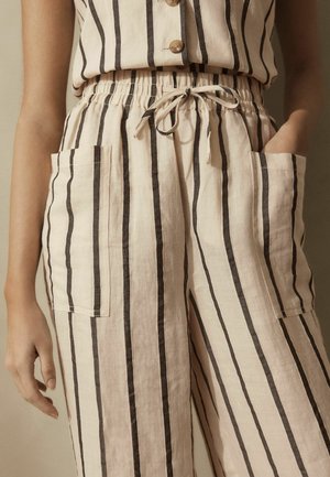 Pantalones de lino ligeros en color crema con rayas verticales en navy, que cuentan con una cintura elástica, cordón ajustable y bolsillos laterales.