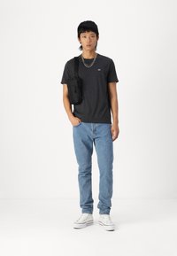 Svart kortermet t-skjorte, grå jeans og hvite sneakers. Modell som holder en liten svart veske. Minimalistisk design med avslappet passform.