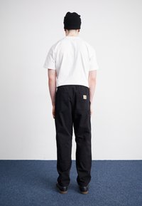 Black cargo pants with a relaxed fit, featuring two back pockets and a small logo patch. White short-sleeve shirt, visible from the back.