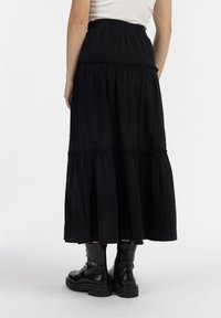 Zwarte maxi-jurk met lagen van een gestructureerde stof, elastische tailleband en gerimpelde naden; gecombineerd met zwarte veters combat boots.
