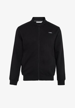 Veste noire zippée avec un col montant, associée à un jean bleu et des baskets blanches, présentant un design élégant et une coupe décontractée.