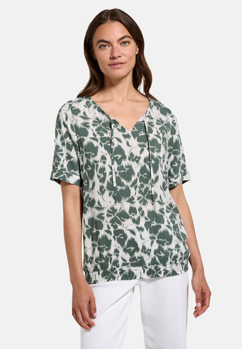 Top corto a maniche corte verde e bianco con scollatura a V, caratterizzato da un motivo a foglia e stringhe regolabili sul collo. Tessuto leggero.