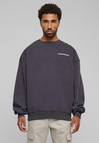 Sudadera gris de gran tamaño con cuello redondo acanalado, hombros caídos y texto blanco "PROHIBIDO" en el pecho; material suave de mezcla de algodón.