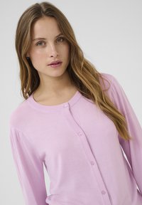 Light pink cardigan made of soft fabric, featuring a round neckline and long sleeves, with a button-down front and ribbed accents.