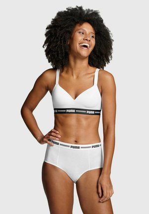 Weißer Bralette mit verstellbaren Trägern und schwarzem Markenbund; kombiniert mit weißen hochgeschnittenen Unterhosen mit passendem Logo-Bund.