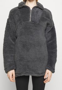 Sudadera gris de forro polar con cuello alto y cierre de media cremallera. Tejido texturizado con un acabado suave y aterciopelado y hombros caídos para un ajuste relajado.